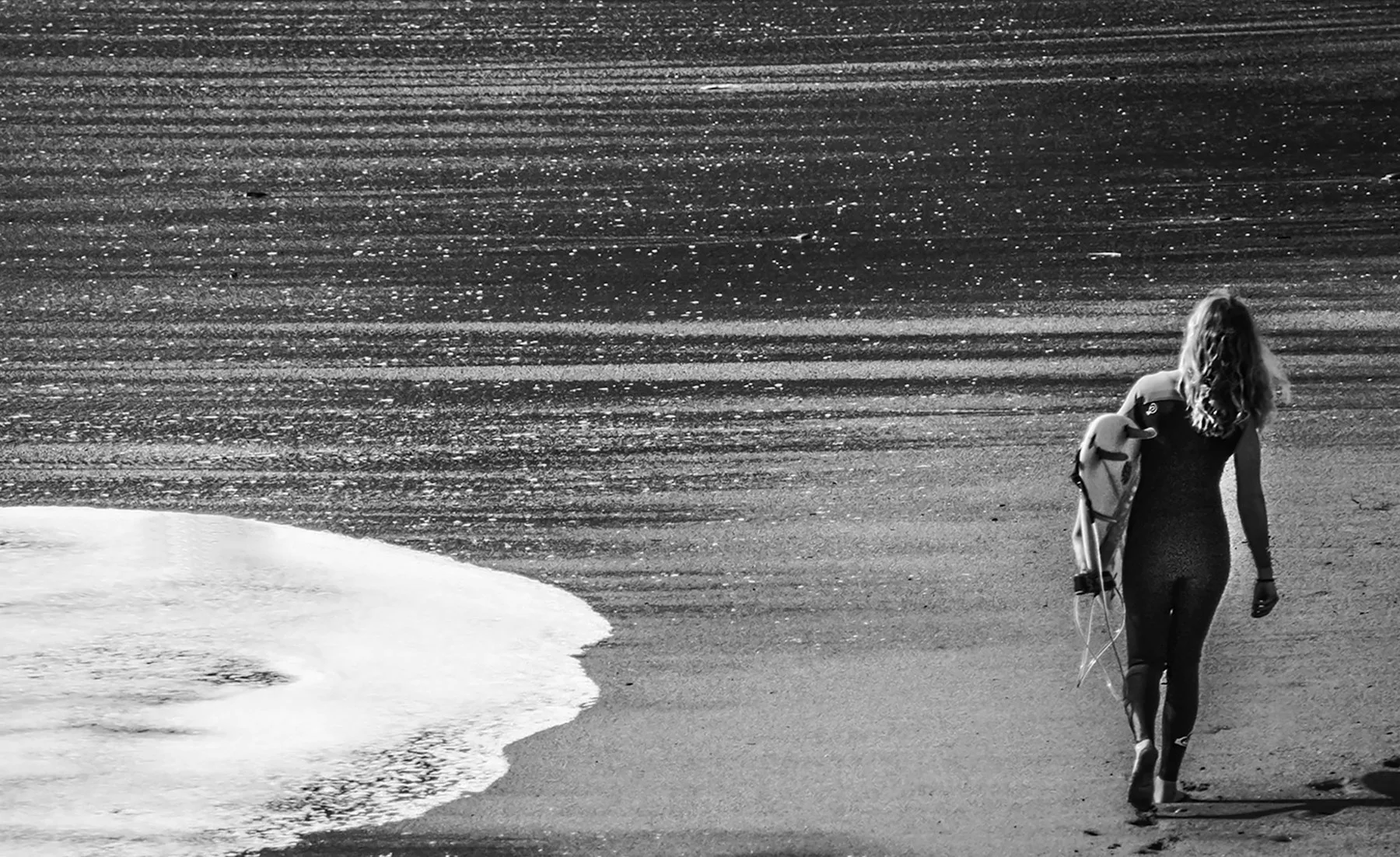 Surfer carrying a board towards the water on a sunlit beach
